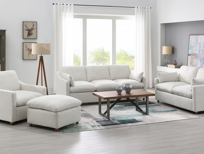 A cream-colored, modern sofa with three cushions and two armrest pillows. The sofa has a minimalist design with short wooden legs and a cozy fabric texture. Set against a plain white background.