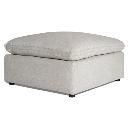 A light gray, fabric ottoman with a large, cushioned top and square base on small black legs, positioned against a white background.