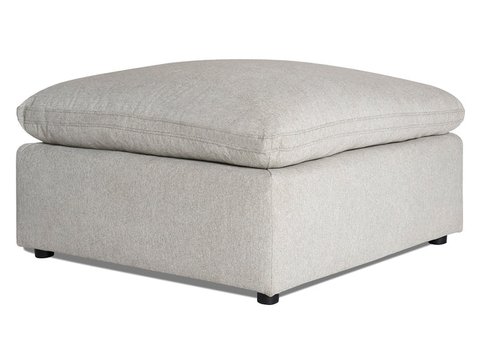 A light gray, fabric ottoman with a large, cushioned top and square base on small black legs, positioned against a white background.