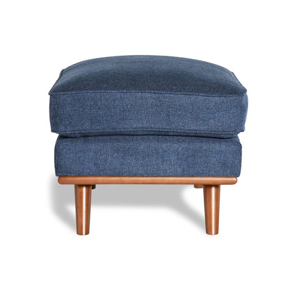 The Maddox Ottoman features a rectangular cushion in blue upholstery and rests elegantly on wooden legs, casting a shadow against a white background—ideal for adding mid-century charm to any living space.