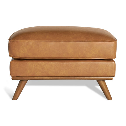 Meet the Maddox Ottoman: a rectangular brown leather piece with four angled wooden legs, complemented by a plush cushion. This cozy yet stylish ottoman adds mid-century modern charm to any living area against a simple white background.