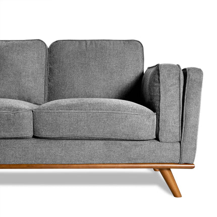 The Maddox is a modern gray fabric sofa with a wooden base and angled legs. It features plush cushions and an armrest, embodying mid-century modern design against a white background, perfect for any living room.