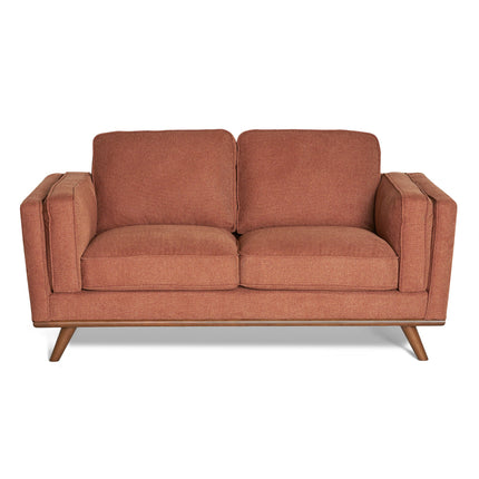 The Maddox Loveseat is a mid-century modern piece offering brownish-red fabric upholstery, square armrests, two seat cushions, and two back cushions. It features durable construction with angled wooden legs for a retro look.