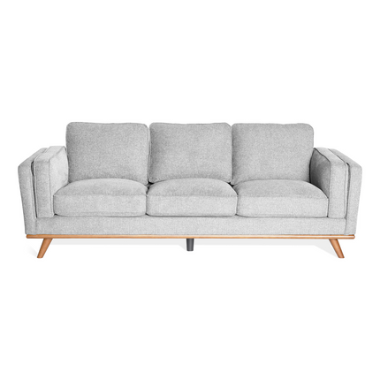 The Maddox Sofa is a modern gray piece with mid-century flair, featuring three plush cushions and sleek wooden legs. Its minimalist design, clean lines, and neutral color make it perfect for contemporary living spaces.